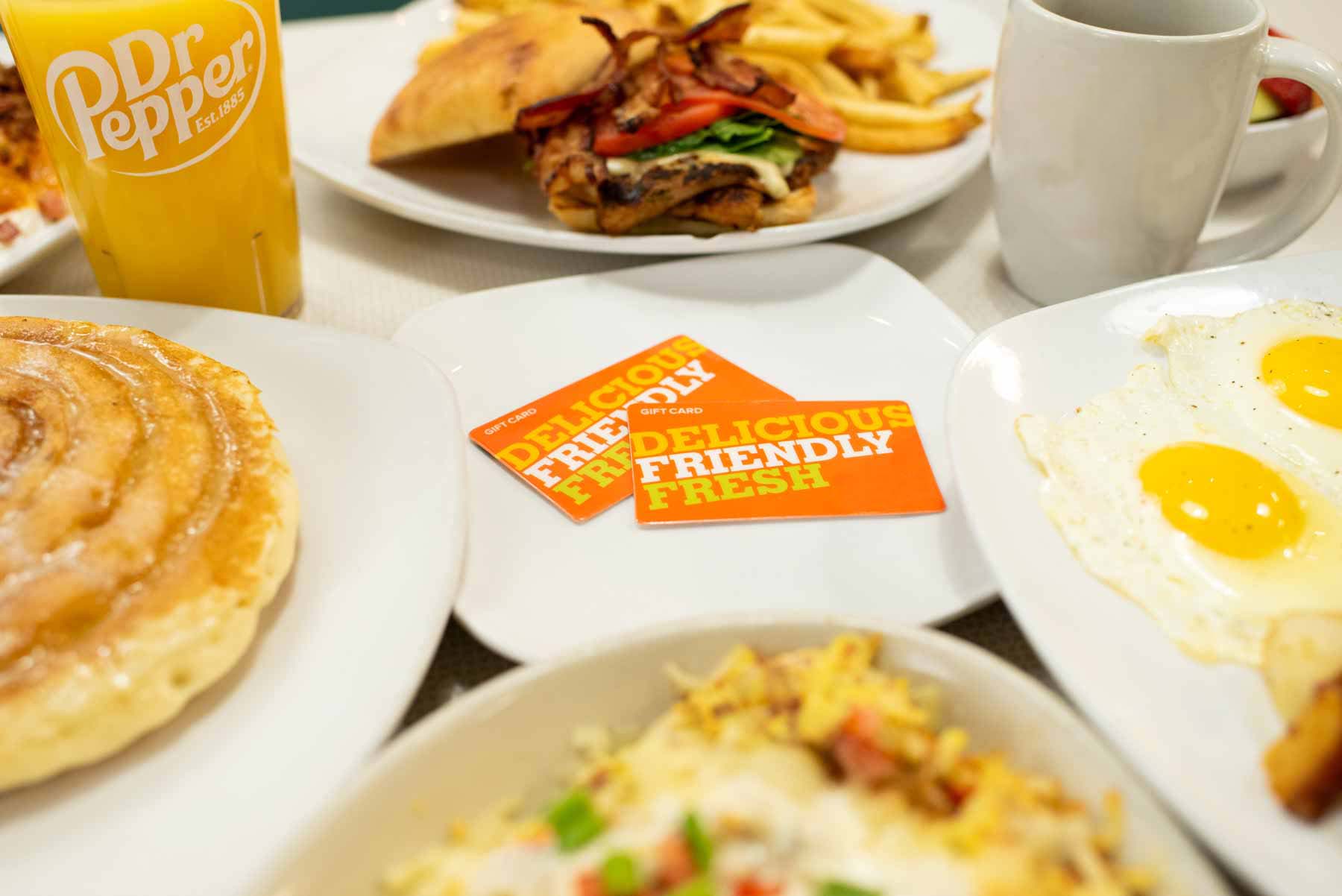The Original Egg gift card with plated breakfast and lunch food is surrounding the gift card on a table.